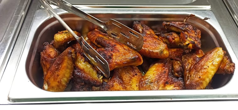 A large tray filled with perfectly grilled chicken wings showcases their rich, golden-brown color and crispy texture, enticing diners with a savory aroma at a lively outdoor gathering.