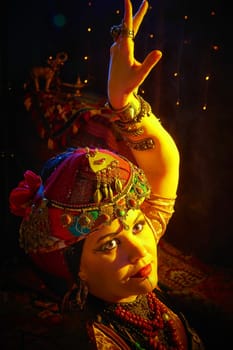 A woman in a colorful headscarf and jewelry poses in front of wall of colorful tassels