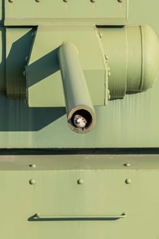 The image captures a detailed view of a military tank's barrel, showcasing its green paint and structural elements, with a hint of light reflecting off the metal surface.