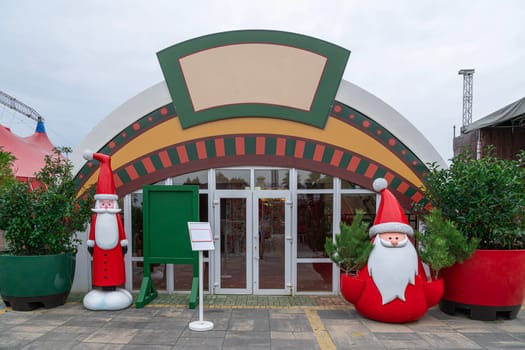 The entrance features large Santa figures flanking both sides, inviting visitors into a festive holiday market decorated with vibrant colors and greenery.