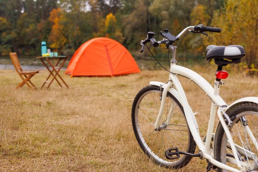 orange tent set up on grassy lake shore, bicycle in front of it, bicycle tourism, green tourism concept