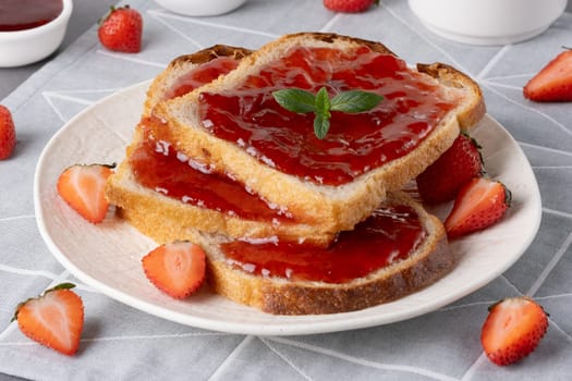 Bread with tasty strawberry jam on grey table.