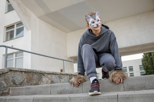 Teenager wearing cat mask and gloves performs quadrobics in the city, imitating the movements of a cat