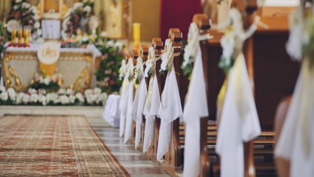 White decorations and flowers are adorning wooden church benches in a church