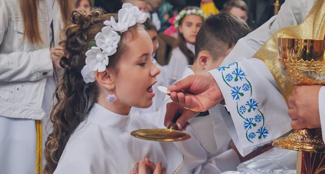 Young girl receiving her first holy communion in a church from a priest