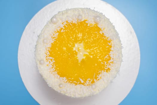 Delicious fresh homemade round coconut cake decorated with orange jelly and coconut chips on blue background