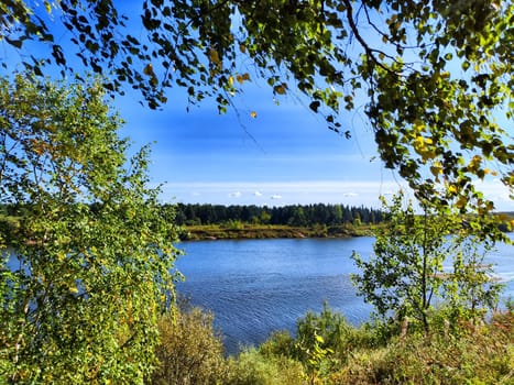 The picturesque river flows gently, surrounded by lush greenery and bathed in sunlight, evoking a peaceful spring atmosphere.