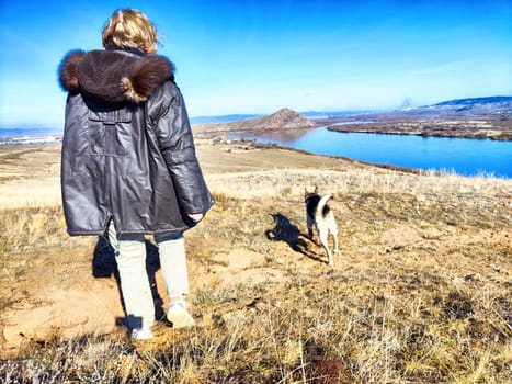 Adult girl with shepherd dog taking selfie near water of lake or river in mountain. Middle aged woman and big pet on nature. Friendship, love and fun