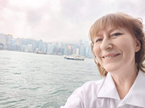 A woman wearing a crisp white shirt is smiling joyfully while standing in front of a serene body of water under a clear sky