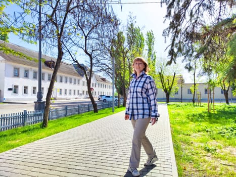 A middle-aged traveler strolls leisurely down sunny pathway lined with trees and quaint architecture