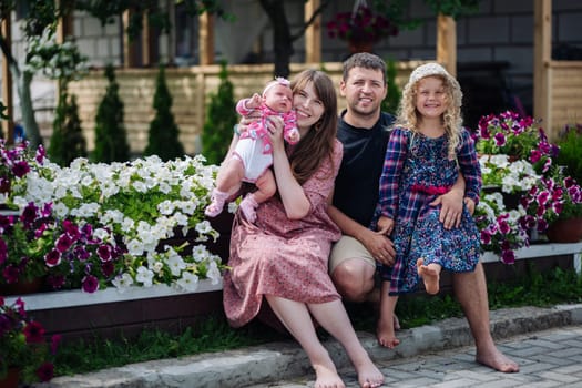 Happy family is sitting in front of their house, posing with their newborn baby girl