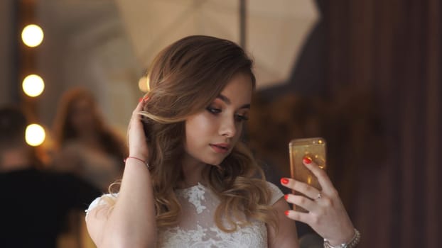 Gorgeous blonde woman with flowing hair is playing with her hair while snapping a selfie with her phone in a room filled with mirrors