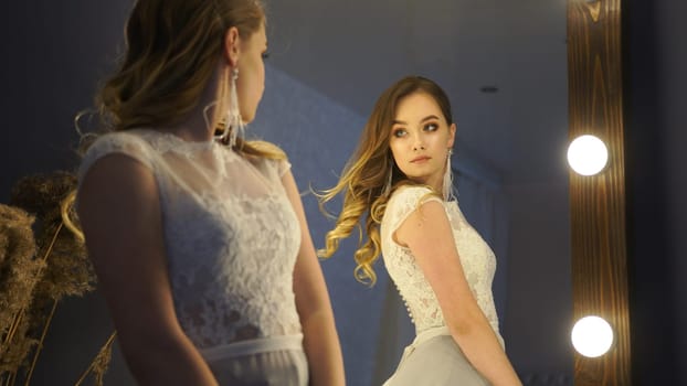 Young woman admiring herself in a mirror while wearing a white lace dress and getting ready for her wedding