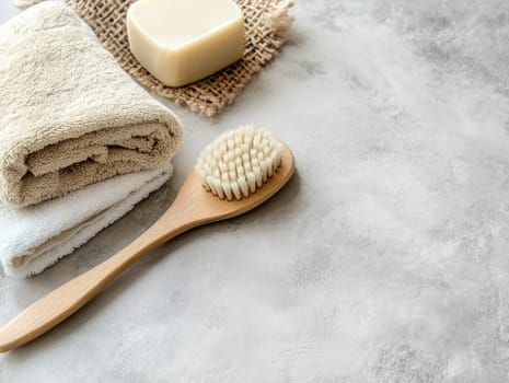 A wooden brush rests beside a bar of soap and neatly folded towels on a soft, textured gray surface. This arrangement showcases a calming, minimalist bathroom atmosphere.