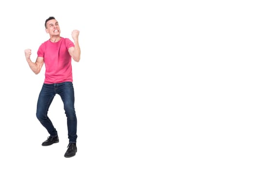 Full length of furious young male with dark hair in t shirt and jeans gritting teeth and clenching fists aggressively while standing against white background