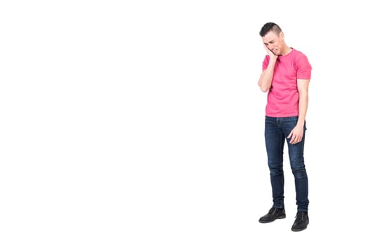 Full body of sorrowful young male with dark hair in casual clothes touching cheek and crying against white background