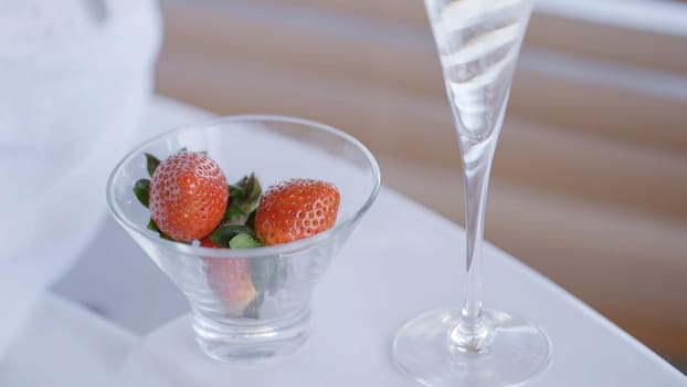 Champagne and strawberries in a glass bowl. Action. Close up of female and male hands taking berries