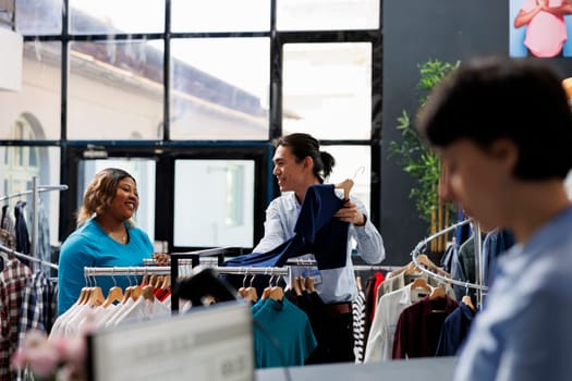 African american customer discussing about casual wear with worker, shopping for stylish merchandise in modern boutique. Shopaholic woman buying fashionable clothes in clothing store