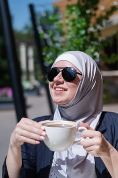 Caucasian woman in hijab drinking coffee in outdoor cafe