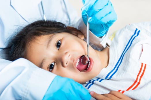 Dental kid health examination. Doctor examines oral cavity of little child uses mouth mirror to checking teeth cavity, Asian dentist making examination procedure for smiling cute little girl