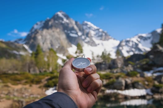 Snow-capped mountains and a tourist hand with an old metal compass in the foreground. Nature reserve, landscape photography.