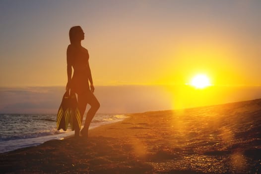 A girl diver holds fins in her hands. Summer vacation. Female sexy body silhouette during sunset on vacation after swimming with fins.