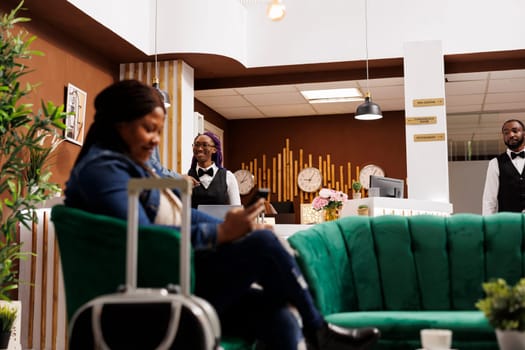 Smiling African American hotel staff standing at front desk welcoming and greeting guests with smile. Friendly female receptionist waiting for tourists, good customer service in hospitality