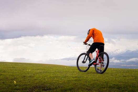 Professional mountain biker on the background of mountains and green hills. Tired mtb rider in full face helmet outdoors.