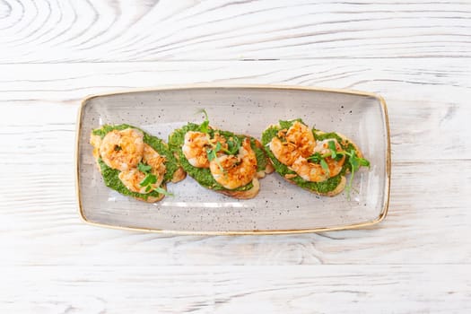 Bruschetta with shrimp on ciabatta toast with avocado cream and pesto sauce. High quality photo