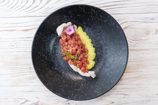 Tuna tartare with avocado on a black plate on a light wooden background. High quality photo