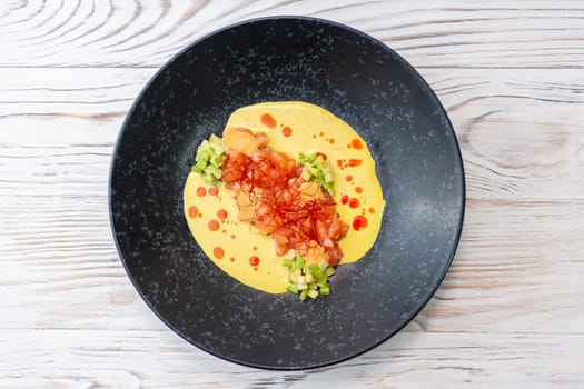 Salmon tartare with avocado lots of sauce and chili threads on a black plate on a light wooden background