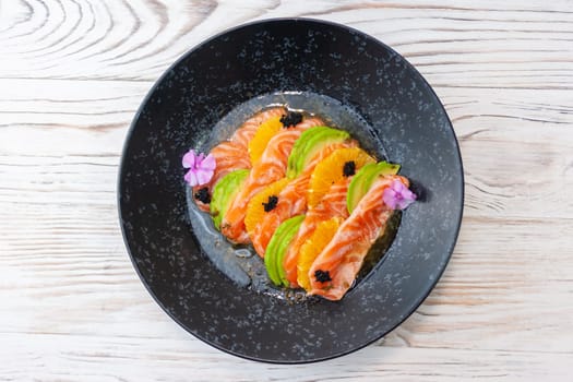 Salmon ceviche with avocado, orange and mango salsa on a light wooden background