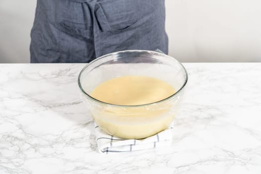 Whisking in a large glass bowl together ingredients to make the white chocolate ganache frosting.