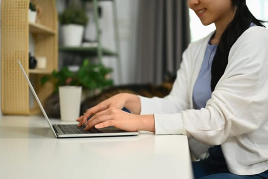 Happy young Asian woman using laptop computer working or studying online at home.