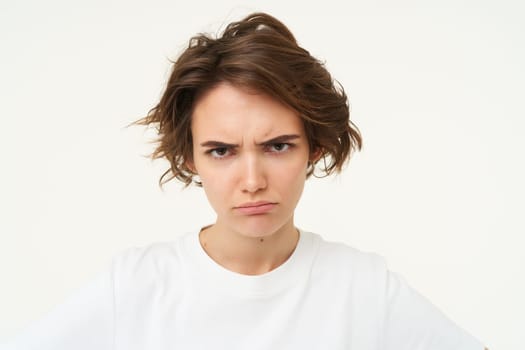 Close up of brunette woman shows angry face, frowning grumpy, pouting and looking disappointed, standing over white background. Copy space