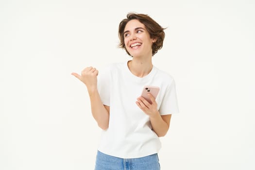Portrait of woman with smartphone, using mobile phone and pointing at banner, showing text advertisement, standing isolated against white background.