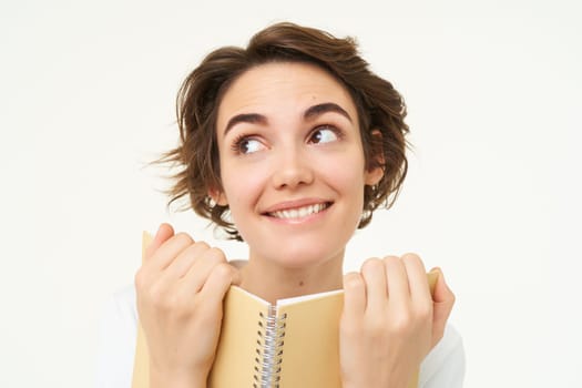 Portrait of happy woman with planner, holding notebook, reading notes and smiling, standing over white background.