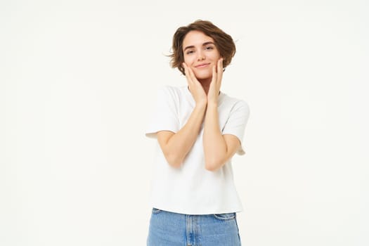 People and lifestyle. Portrait of smiling, gentle young brunette woman, gazing at camera, looking at something lovely, standing over white studio background.