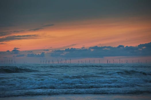 Wind turbines in the North Sea in Netherlands at sunset.