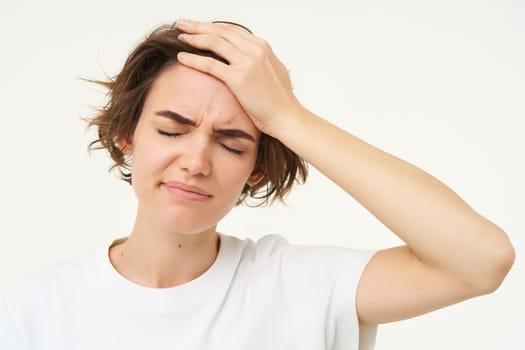 Portrait of woman touches her head, looks upset or disappointed, forgot something, has headache, migraine, standing over white background.