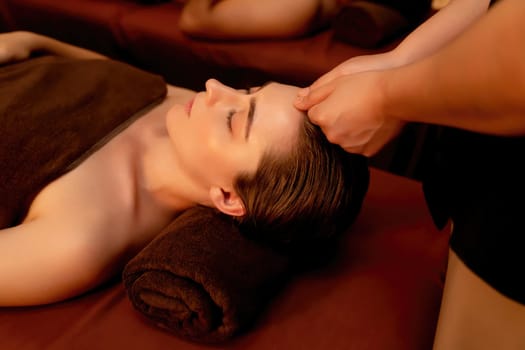 Couple customer enjoying relaxing anti-stress head massage and pampering facial beauty skin recreation leisure in warm candle lighting ambient salon spa in luxury resort or hotel. Quiescent