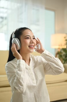 Beautiful young Asian woman enjoying music over headphones while relaxing at home.
