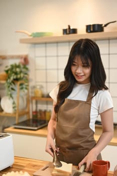 Young beautiful woman wearing apron preparing breakfast at the kitchen.
