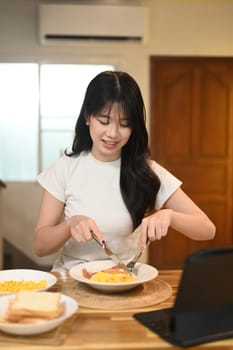 Charming young woman in casual clothes enjoying breakfast in a modern kitchen.