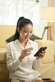 Young Asian woman holding credit card and using mobile phone for financial transaction.