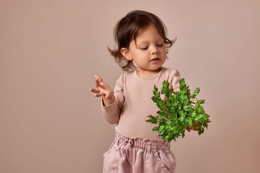 smiling child girl holding fresh green parsley on beige background. healthy baby food.