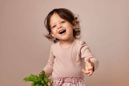smiling very excited child girl holding fresh green salad on beige background. healthy baby food.