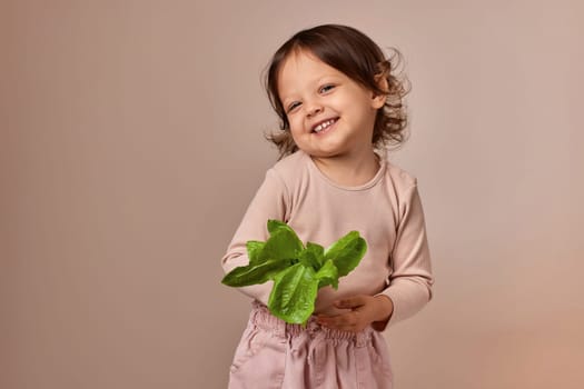 smiling child girl holding fresh green salad on beige background. healthy baby food.