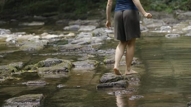 A girl in puffy shorts in nature.Creative.A young woman jumps on stone through a stream in the jungle. High quality 4k footage