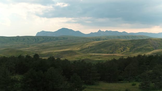 Beautiful mountain landscape with green hills and rocks on horizon. Shot. Top view of green trees on background of hills and mountains on horizon.